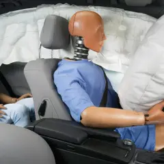 Manekin w samochodzie podczas testu zderzeniowego, z wystrzelonym airbagiem chroniącym kierowcę.