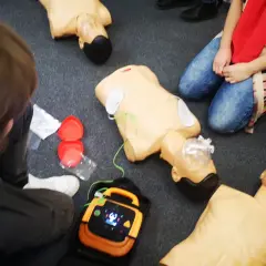 Uczestnicy kpp kursu ćwiczą resuscytację na fantomach. Widać defibrylator i akcesoria do RKO.