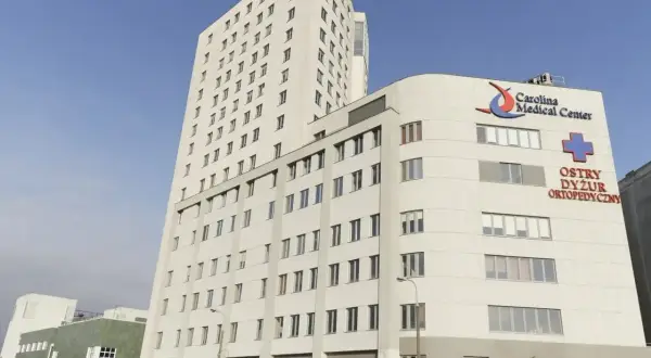 Nowoczesny budynek Carolina Medical Center w Warszawie z niebieskim krzyżem i napisem "Ostry Dyżur Ortopedyczny".