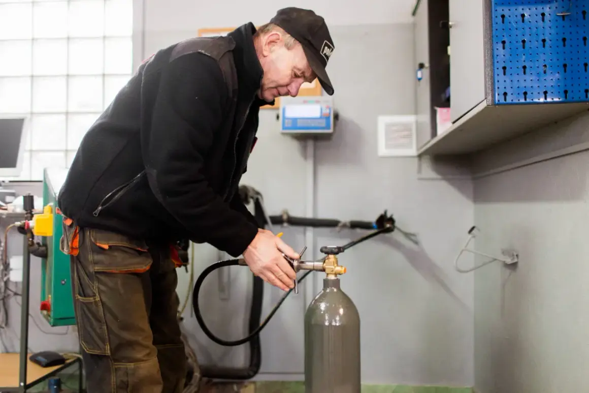 Pracownik w czapce i roboczych spodniach dokonuje napełniania butli CO2, podłączając wąż do zaworu.