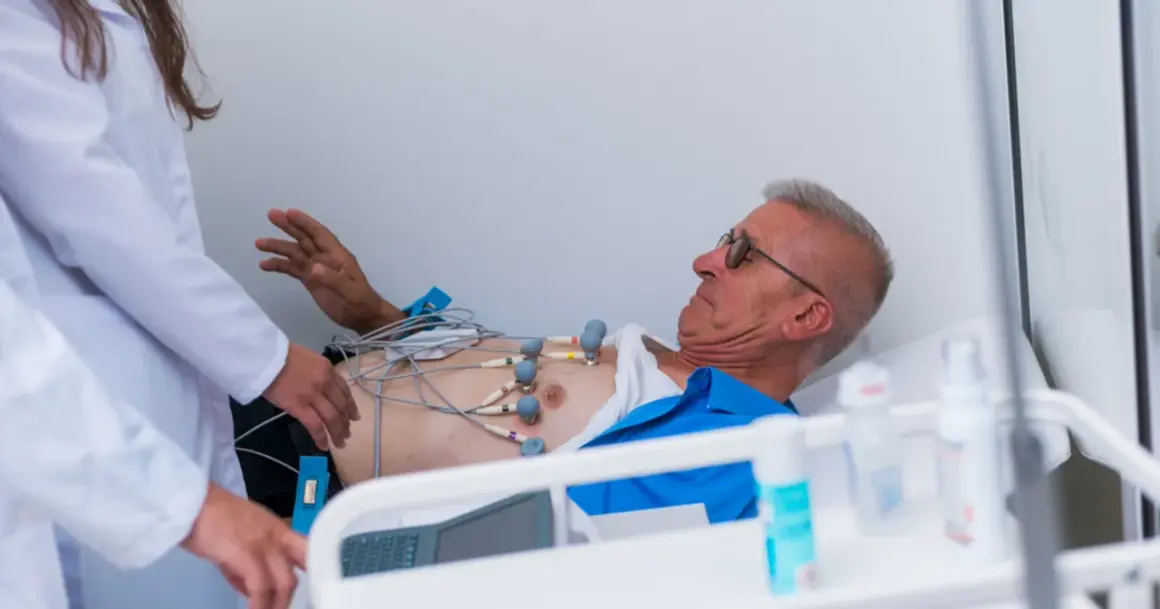 Mężczyzna z elektrodami EKG na klatce piersiowej, pod opieką lekarzy, w stanie przedzawałowym.