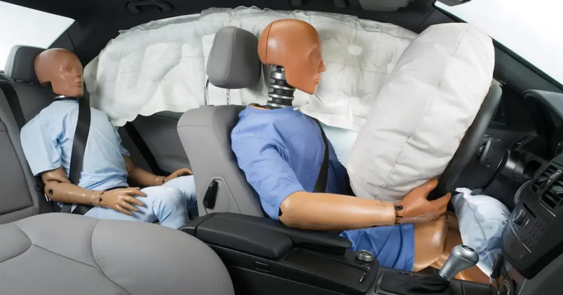 Manekin w samochodzie podczas testu zderzeniowego, z wystrzelonym airbagiem chroniącym kierowcę.