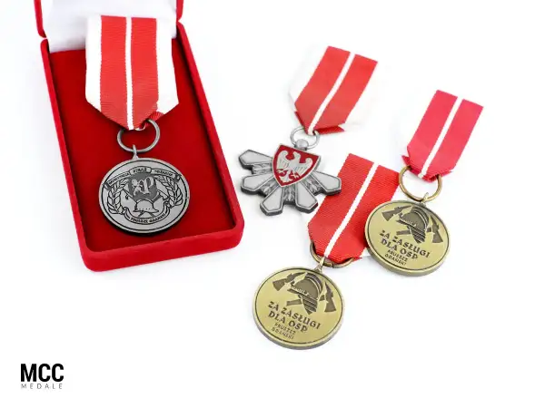 Odznaczenia strażackie w pudełku i luźno leżące na białym tle. Widać godło Polski i symbole strażackie.